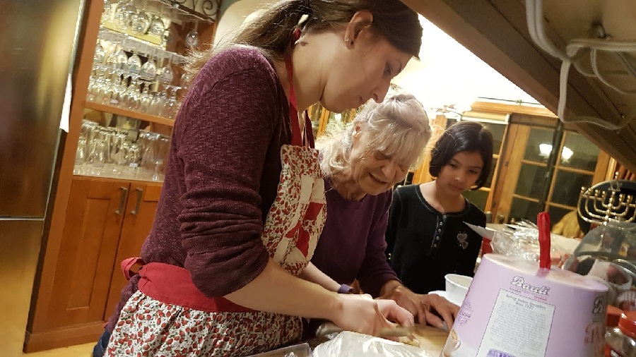 Two women, one in her 70s, one in her 30s, cook alongside a little girl. 