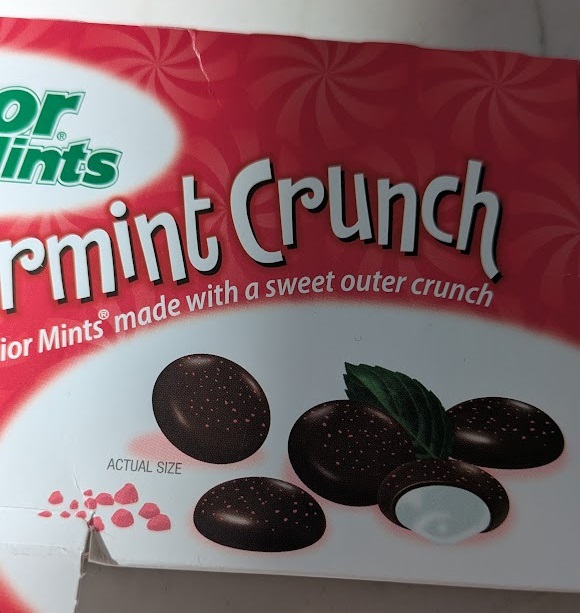 The packaging for box of Junior Mints that shows the candies as having little red freckles on them. 